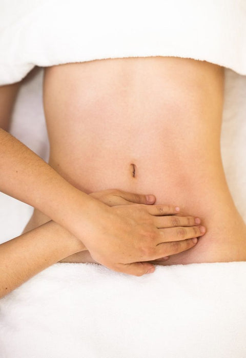 Close-up of a person's hand giving a massage on client's stomach against a white background